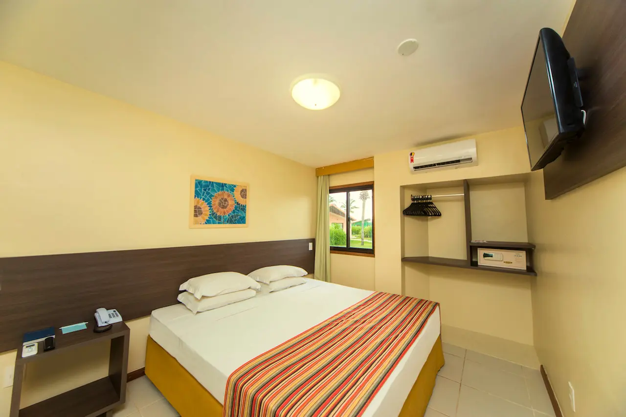 Quarto do bangalô com cama de casal, TV, ar-condicionado e colcha listrada