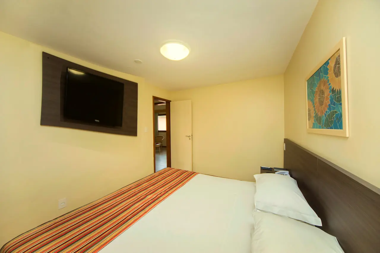 Quarto do bangalô com cama de casal, TV na parede e quadro de flores