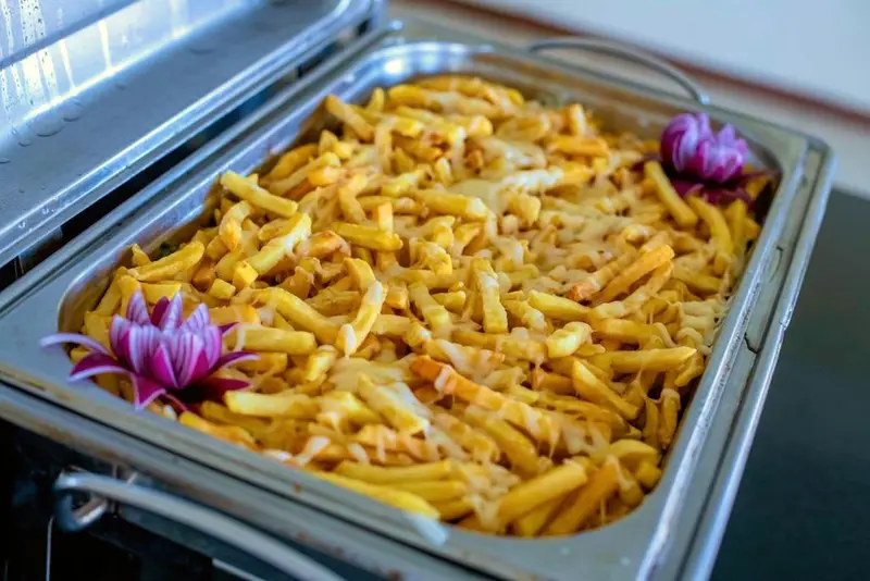 Batatas fritas gratinadas com queijo na cuba do bufê, com flor de cebola roxa