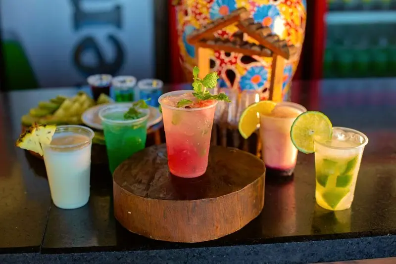 Mesa com copos de drinks coloridos, limão e hortelã sobre um tronco de madeira