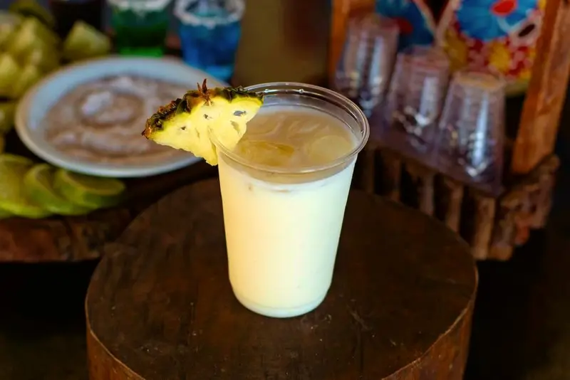 Copo de bebida cremosa com fatia de abacaxi sobre um tronco de madeira