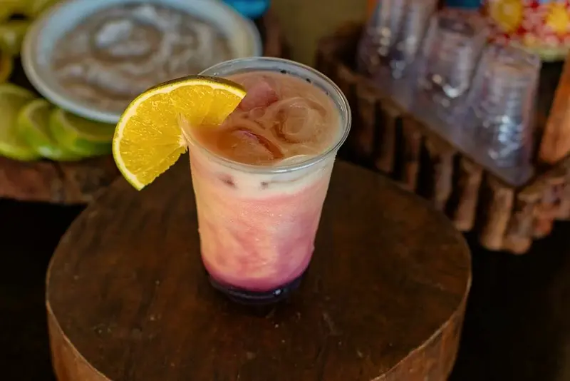 Drink gelado rosado com fatia de laranja sobre um tronco de madeira