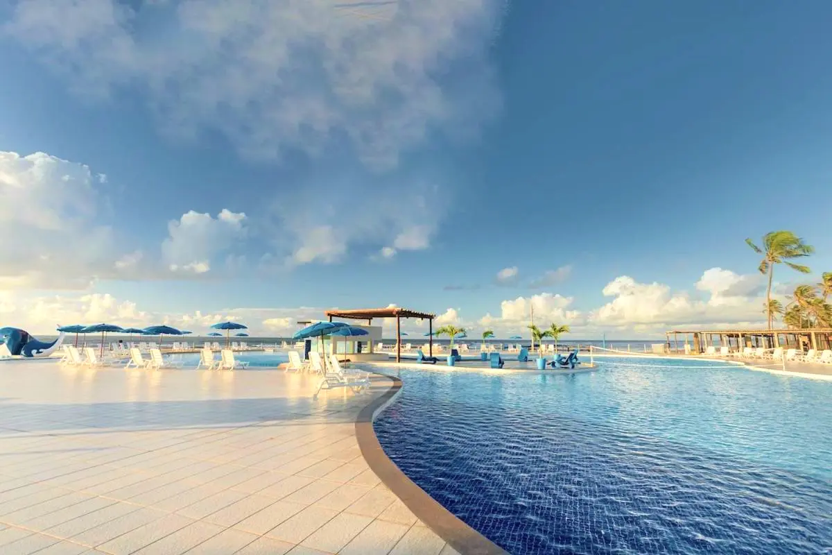 Borda curva da piscina com guarda-sóis e o céu com nuvens ao fundo