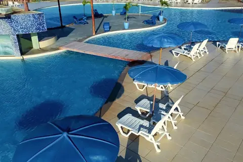Piscina com deck, guarda-sóis azuis e espreguiçadeiras brancas vista do alto