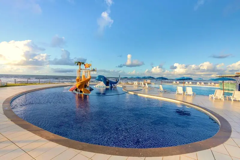 Piscina infantil redonda com escorregador de baleia e brinquedos, vista de frente para o mar