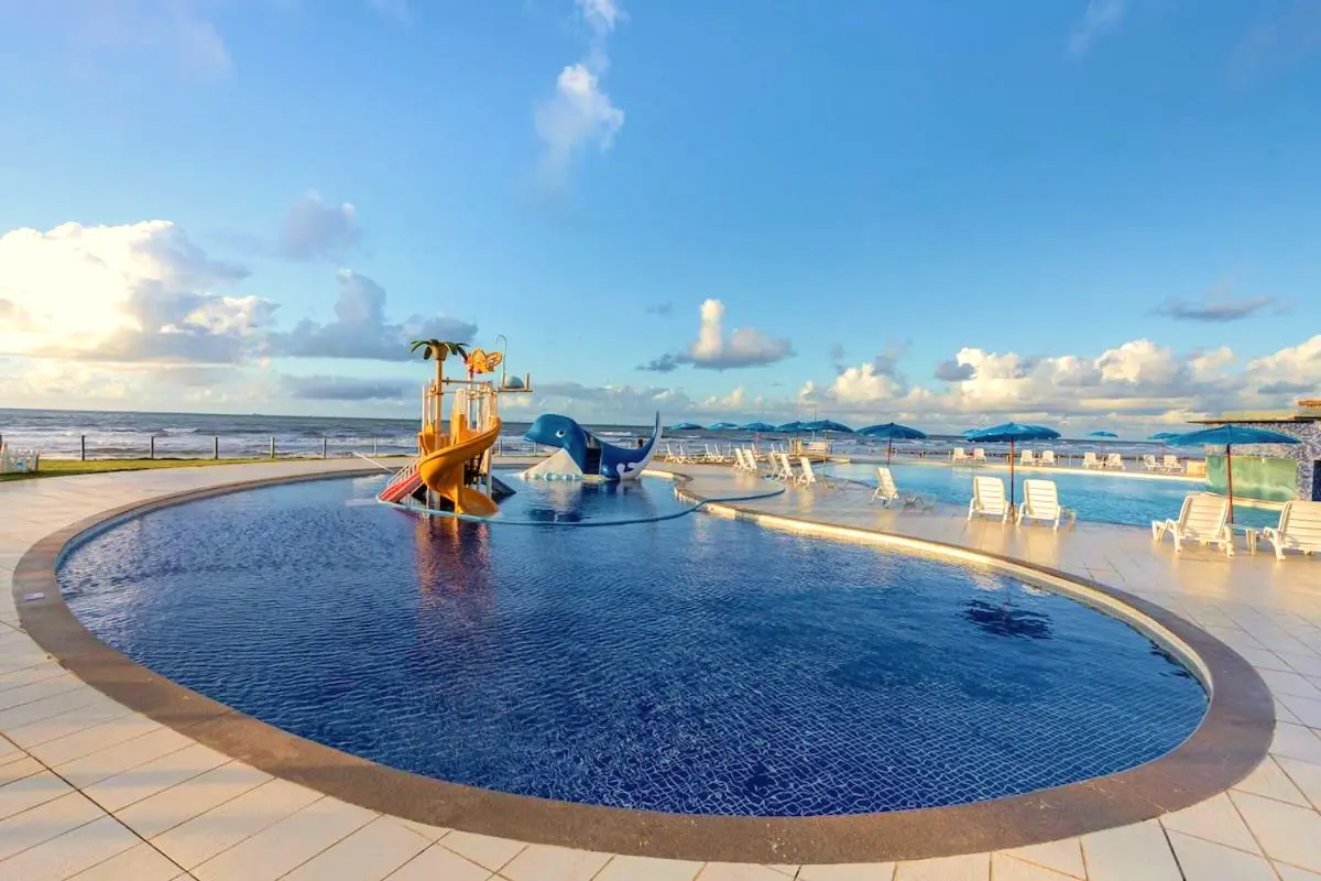 Piscina infantil redonda com escorregador de baleia e brinquedos, vista de frente para o mar