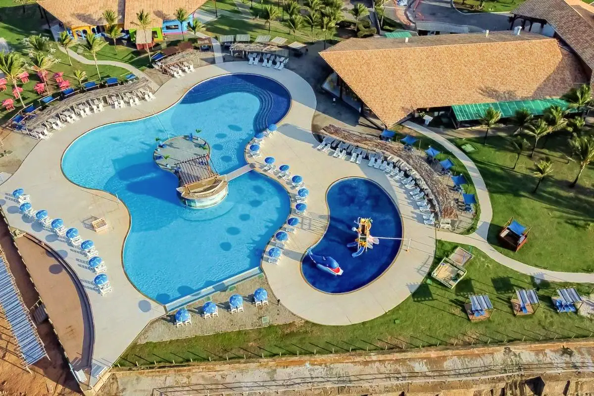Vista aérea das piscinas de curvas com quiosque de palha, deck e gramado ao redor