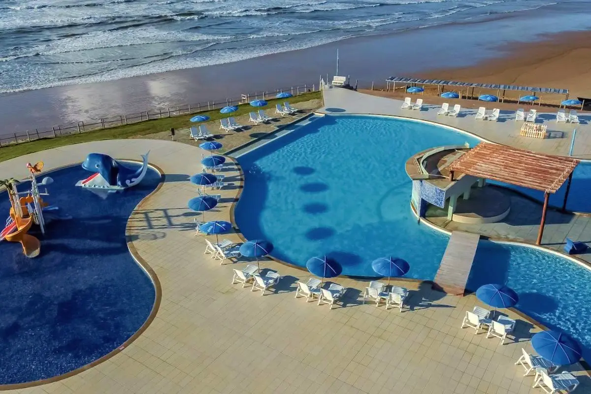 Vista aérea da piscina de curvas com guarda-sóis, a praia e o mar ao lado