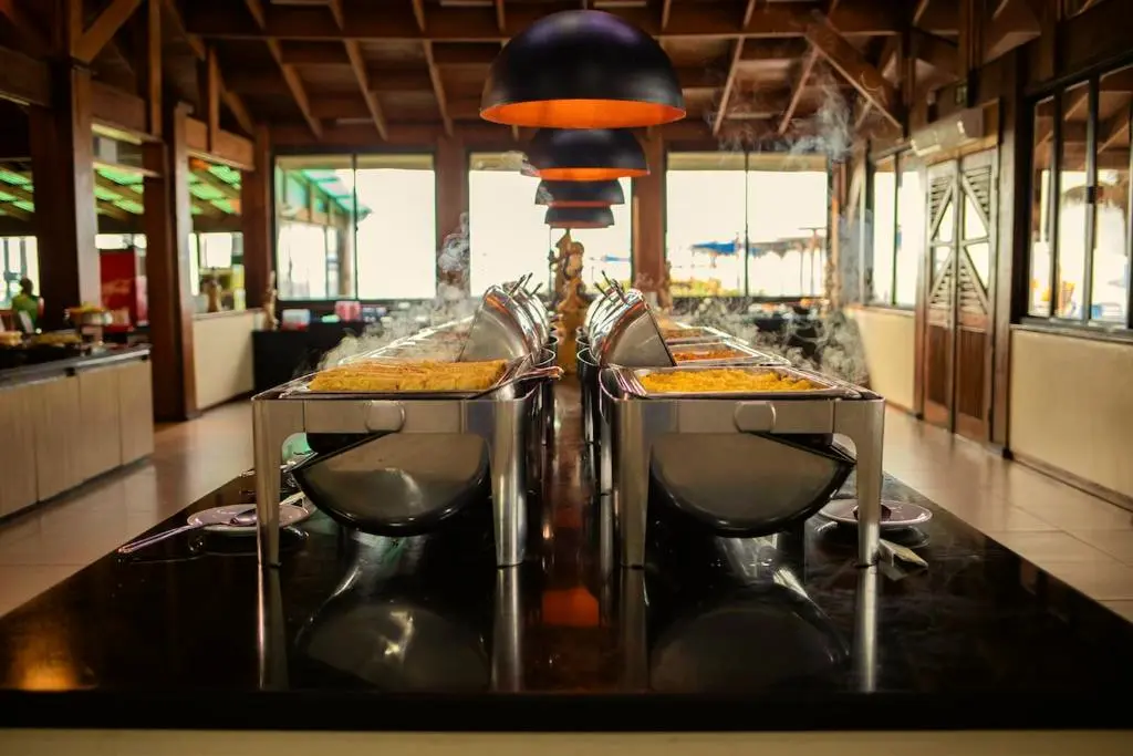 Restaurante com bufê em ilha central, cubas fumegantes e luminárias pretas