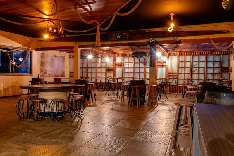 Salão de madeira com cordas decorativas, mesas e bancos altos